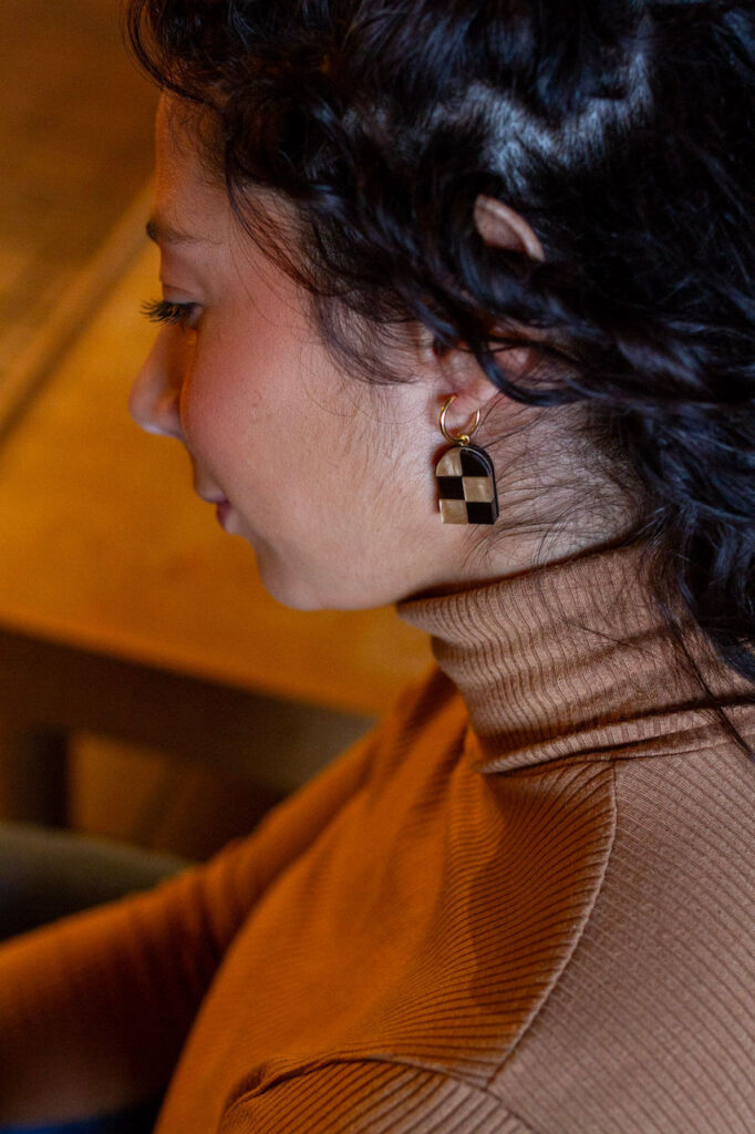 Close up of woman wearing brown and gold checkered arch earrings