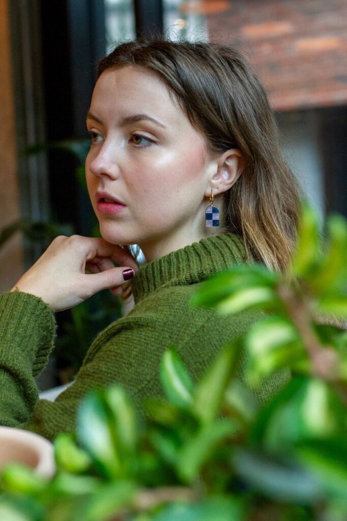 Woman wearing purple checkered earrings which foliage in foreground