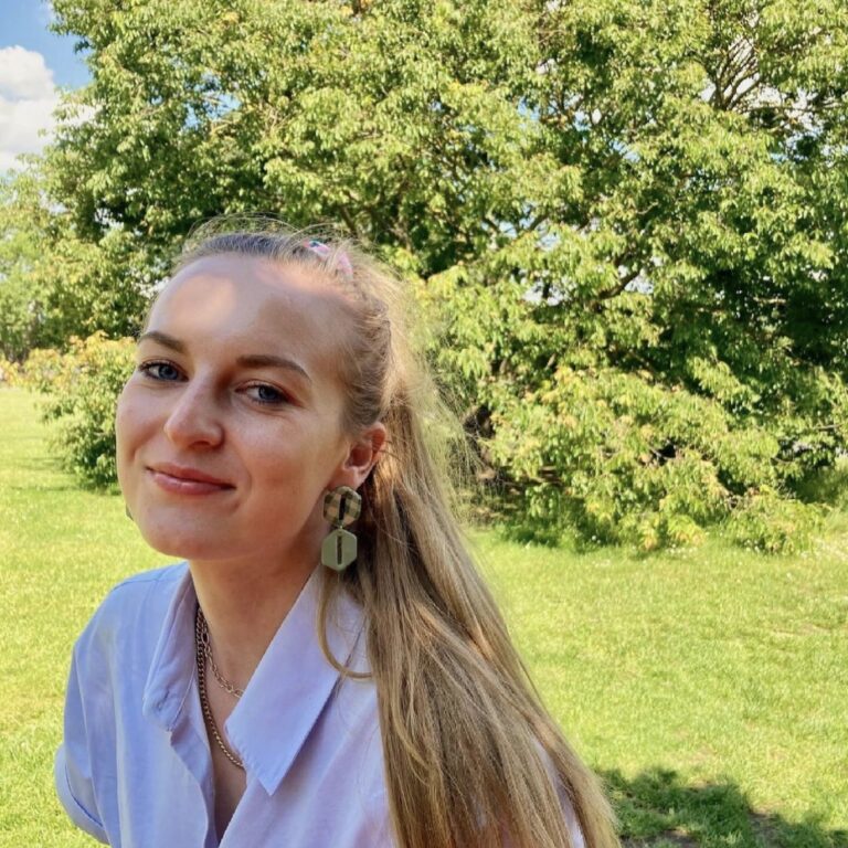 Woman wearing green checkered earrings with trees in background